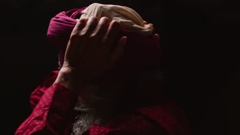 Close-Up-Low-Key-Studio-Lighting-Shot-Of-Senior-Sikh-Man-With-Beard-Using-Salai-Needle-When-Putting-On-Turban-Against-Dark-Background-1